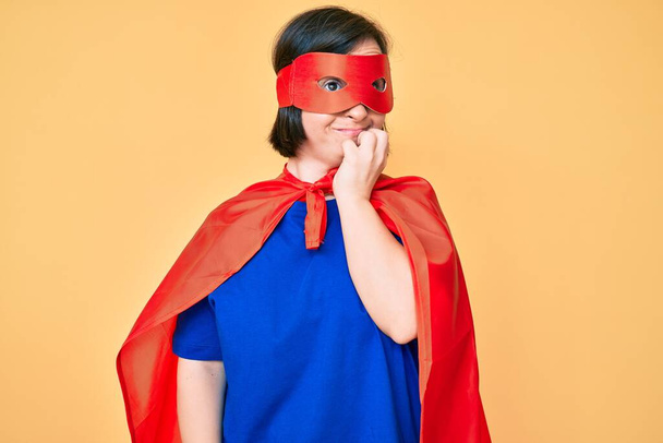 Brunette woman with down syndrome wearing super hero costume looking stressed and nervous with hands on mouth biting nails. anxiety problem.  - Foto, Bild