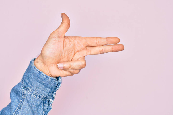 Hand van Kaukasische jongeman met vingers over geïsoleerde roze achtergrond gebaren vuurwapen met vingers, richten schieten symbool - Foto, afbeelding
