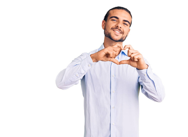 Jeune homme beau portant des vêtements de travail souriant dans l'amour faisant forme de symbole de coeur avec les mains. concept romantique.  - Photo, image
