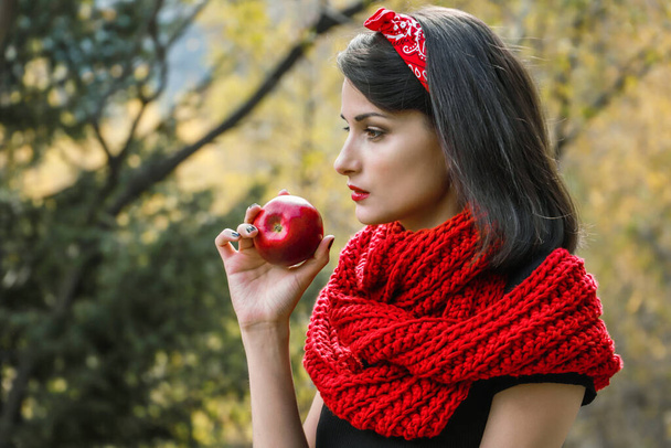 Большое спелое яблоко в руке женщины на фоне красного шарфа - Фото, изображение