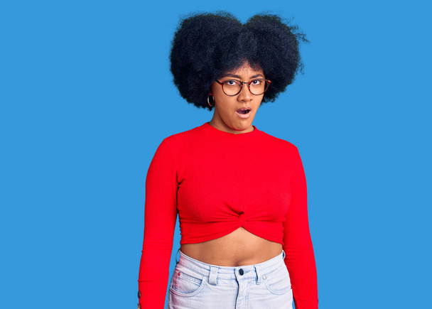 Chica afroamericana joven con ropa casual y gafas en la cara de choque, con aspecto escéptico y sarcástico, sorprendido con la boca abierta  - Foto, Imagen