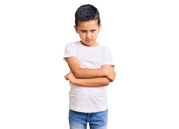 Kleine süße Junge in lässigem weißen T-Shirt skeptisch und nervös, missbilligenden Gesichtsausdruck mit verschränkten Armen. Negative Person.  - Foto, Bild