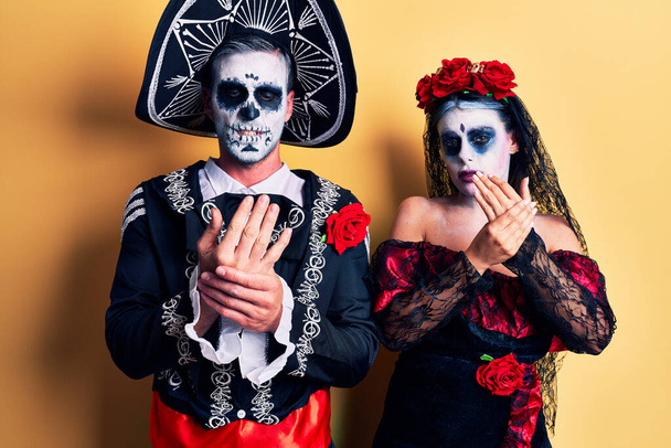 Junges Paar trägt mexikanisches Totenkostüm über gelbem Leiden an Händen und Fingern, Arthritis-Entzündung  - Foto, Bild