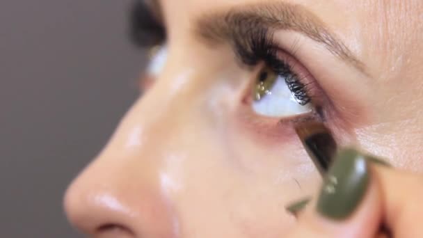 σε ένα σαλόνι ομορφιάς, ένας επαγγελματίας αισθητικός εφαρμόζει eyeliner στο κάτω βλέφαρο του ματιού του κοριτσιού. Κοντινό πλάνο βίντεο του επαγγελματία καλλιτέχνη μακιγιάζ με μαλακό λεπτό πινέλο μακιγιάζ ματιών - Πλάνα, βίντεο