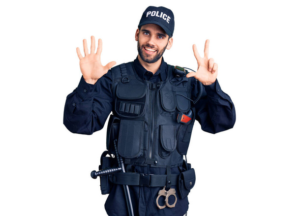 Νεαρός όμορφος άντρας με γενειάδα, με αστυνομική στολή να δείχνει και να δείχνει με τα δάχτυλα νούμερο οκτώ, χαμογελώντας σίγουρος και χαρούμενος..  - Φωτογραφία, εικόνα