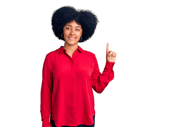 Genç Afro-Amerikan kızı günlük kıyafetler giyip bir numaralı parmağını gösterip gülümserken kendinden emin ve mutlu..  - Fotoğraf, Görsel