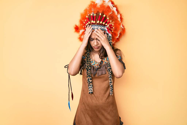 Young beautiful latin girl wearing indian costume suffering from headache desperate and stressed because pain and migraine. hands on head.  - Foto, Bild