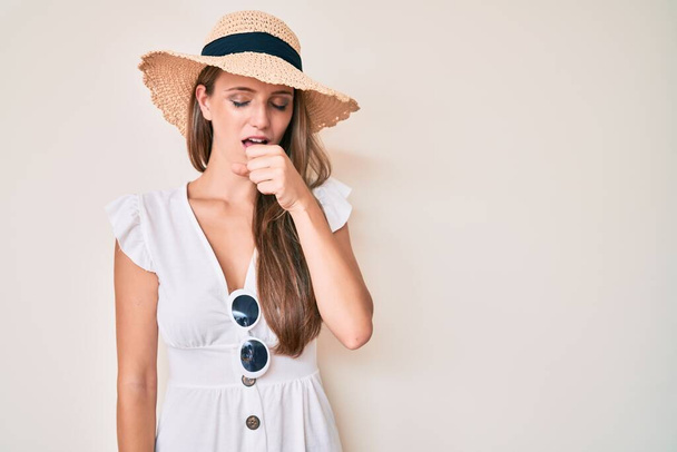 Menina loira jovem usando chapéu de verão sentindo-se mal e tosse como sintoma de frio ou bronquite. conceito de cuidados de saúde.  - Foto, Imagem