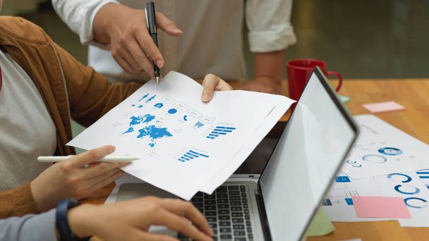 Вид збоку бізнесменів, що аналізують бізнес-чарти з маком на ноутбуці та папері на столі для зустрічей
 - Фото, зображення