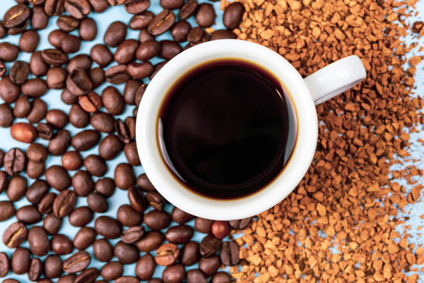 Kávébab félig instant kávéval, középen egy csésze kávé kék háttérrel közelről - Fotó, kép