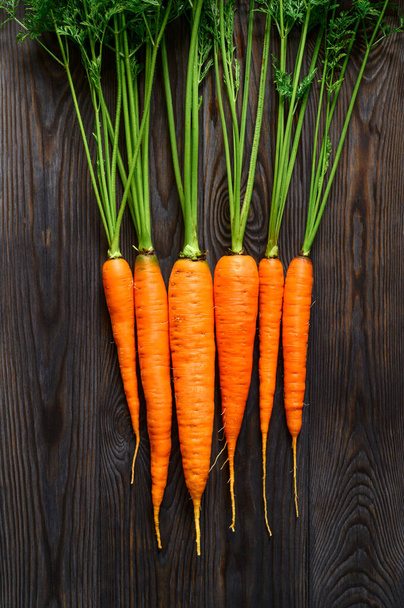 Un ramo de zanahorias crudas con tapas verdes sobre un fondo de madera oscura. Alimentos ecológicos. - Foto, imagen