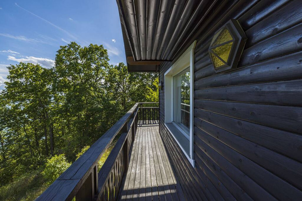 Pohled na fasádu typického dřevěného švédského domu s dřevěnou terasou a zábradlím na pozadí lesa za letního slunečného dne. - Fotografie, Obrázek