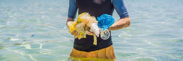 Man collects packages from the beautiful turquoise sea. Paradise beach pollution. Problem of spilled rubbish trash garbage on the beach sand caused by man-made pollution and environmental, campaign to - Foto, Imagen