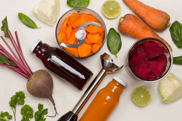Chopped beets in jar, chopped carrots in blender jar. Beets with tops and unpeeled carrots. Metal shredder. Cabbage and lemon halves, basil and parsley. Flat lay. White background. Copy space - Fotó, kép