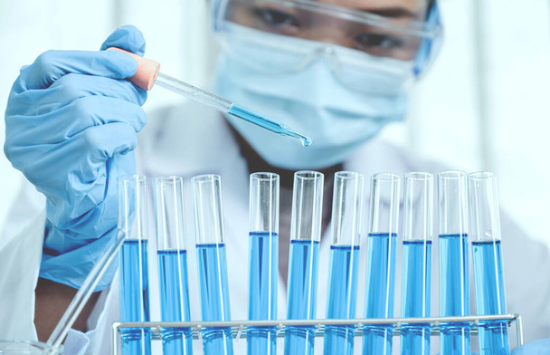 科学者はピペットを保持し、研究室での研究と分析のための青い化学液体をドロップ. - 写真・画像