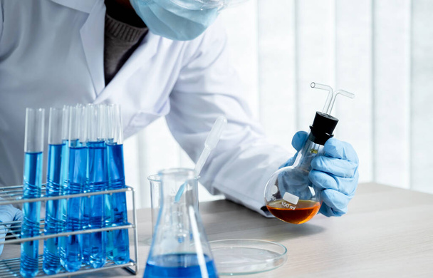 Οι επιστήμονες κρατούν ένα γυάλινο σωλήνα γεμάτο με πορτοκαλί χημικό υγρό για έρευνα και ανάλυση σε ένα εργαστήριο. - Φωτογραφία, εικόνα