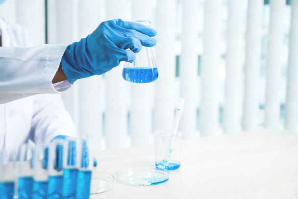 Οι επιστήμονες κρατούν ένα γυάλινο σωλήνα γεμάτο με μπλε χημικό υγρό για έρευνα και ανάλυση σε ένα εργαστήριο. - Φωτογραφία, εικόνα
