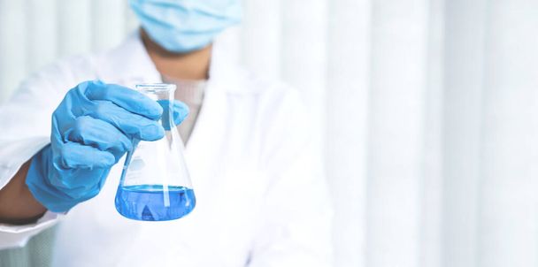 Wetenschappers houden een glazen buis gevuld met blauwe chemische vloeistof voor onderzoek en analyse in een laboratorium. - Foto, afbeelding