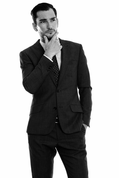 Studio shot of young handsome bearded businessman in suit isolated against white background in black and white - Foto, afbeelding