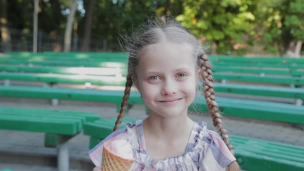 Menina feliz bonita comer sorvete no parque em um banco. - Filmagem, Vídeo