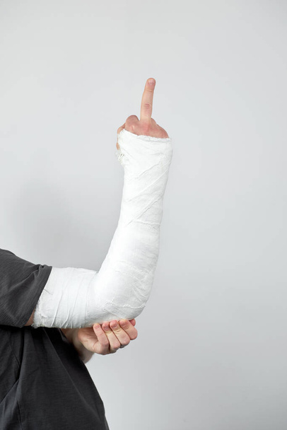 Man with plaster cast on his hand showing sing fuck you on a white wall background. Closeup view. - Fotografie, Obrázek