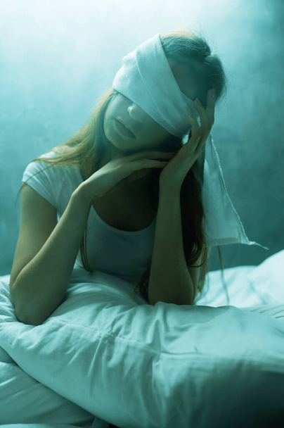 Blindfolded crazy woman sitting in bed, dark room on background. Psychedelic female person having problems every night, depression and stress, sadness, psychiatry hospital - Photo, image