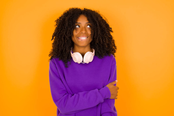   shy  Young beautiful African American woman wearing purple knitted sweater  against yellow  background.   - Foto, afbeelding