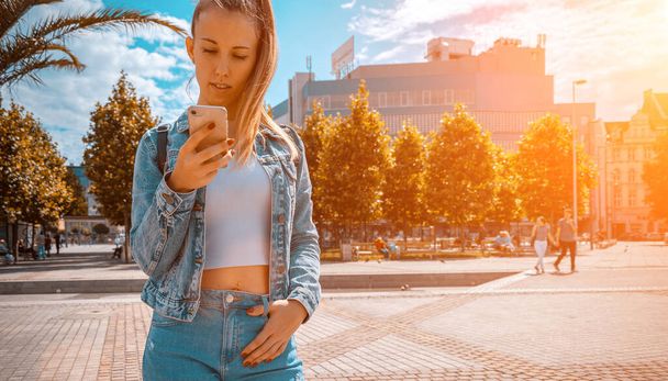 Taking picture. Happy young girl with phone smile, typing texting and taking selfie in summer sunshine urban city. Pretty female taking fun self portrait photo. Vanity, social network concept. - Photo, image