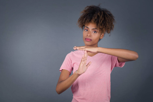 Young beautiful African American woman  tired and bored, making a timeout gesture, needs to stop because of work stress, time concept. Standing against gray wall. - Fotoğraf, Görsel