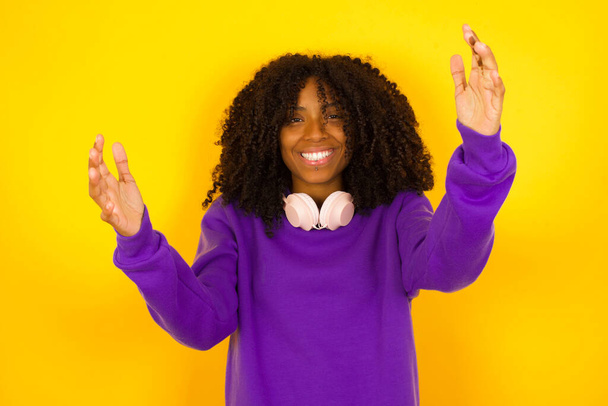 Африканська американка сміється, піднявши руки на жовтому тлі. Поняття емоцій і жестів - Фото, зображення