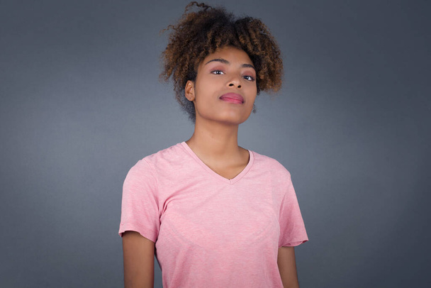 Close up studio shot of Young beautiful African American woman with curly dark hair looking at camera with charming cute smile while posing against white blank copy space wall for your content - 写真・画像
