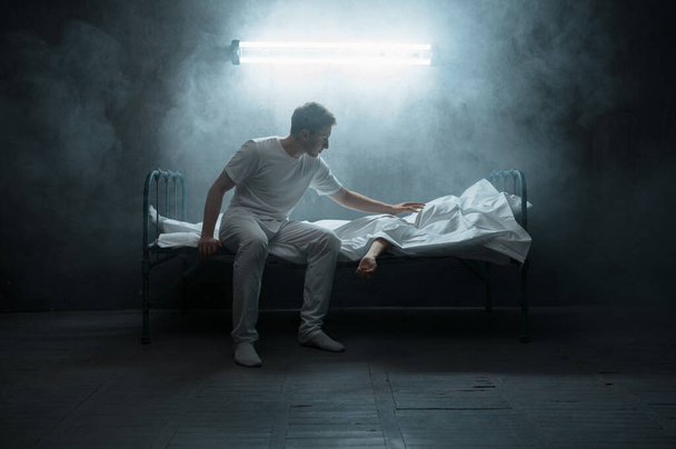 Sad psycho man looking on dead woman in bed, dark room on background. Psychedelic person having problems every night, depression and stress, sadness, psychiatry hospital - Foto, Imagem