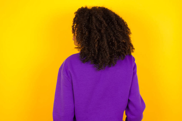 Vista trasera femenina afroamericana sobre fondo amarillo. Concepto de emociones y gestos - Foto, imagen