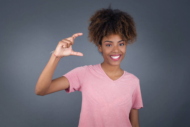 Young beautiful African American woman over isolated background gesturing with hand showing small size, measure symbol. Smiling looking at the camera. Measuring concept. - Foto, immagini