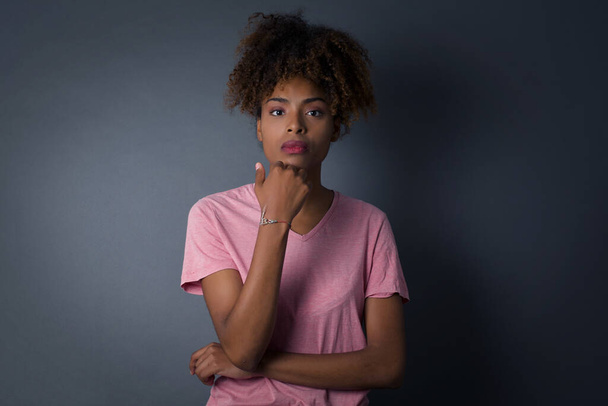 Isolated portrait of stylish African American dark-haired woman with hand near face and looking to the camera with doubtful and skeptical expression suspect and doubt. Isolated over gray background. - Foto, Imagen