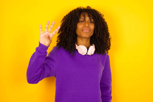 Femme afro-américaine montre quatre doigts sur fond jaune. Concept d'émotions et de gestes - Photo, image