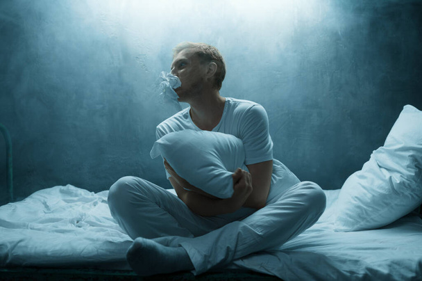 Psycho uomo abbraccia cuscino a letto, orrore insonnia, camera oscura su sfondo. Persona di sesso maschile psichedelico che ha problemi ogni notte, depressione e stress, tristezza, ospedale psichiatrico - Foto, immagini