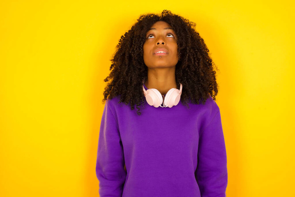 Mujer afroamericana mira hacia arriba en el fondo amarillo. Concepto de emociones y gestos - Foto, Imagen