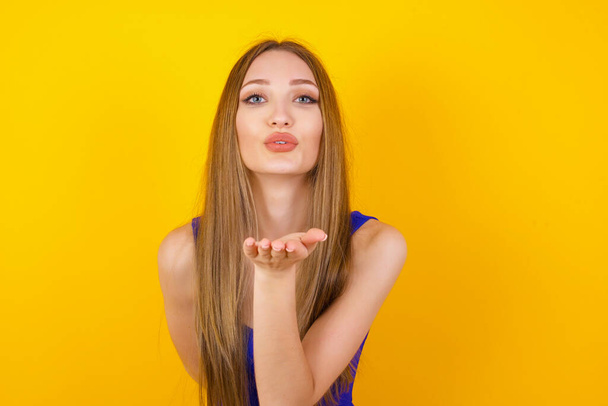 Cute appealing female blows kiss at camera, demonstrates love to boyfriend or says goodbye on distance, isolated over white studio background. Attractive young woman shows sympathy to someone. - Fotografie, Obrázek
