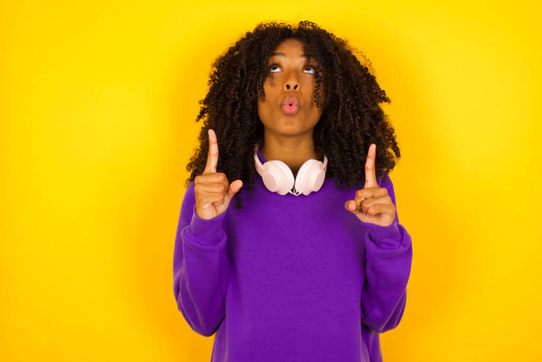 Молода красива афроамериканка у фіолетовому в'язаному светрі, що вказує на жовтий фон.   - Фото, зображення