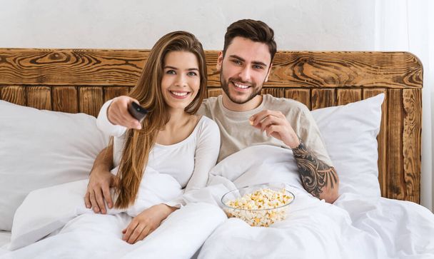 Entertainment in evening. Smiling man eating popcorn, woman presses button on remote control - Fotó, kép