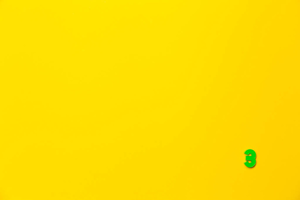 Nummer 3, drei, die dritte der babygrünen Plastikspielzeugnummer befindet sich in der unteren rechten Ecke auf einem gelben Papierhintergrund. Banner zum Thema Seitennummerierung, Timing oder Tag im Kalender. - Foto, Bild