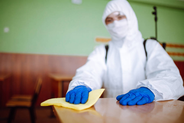 Dezenfeksiyon grubundan bir adam okuldaki masayı sarı bir bezle temizliyor. Profesyonel işçi, covid-19 'un yayılmasını önlemek için sınıfı sterilize ediyor. Öğrencilerin ve öğrencilerin sağlık hizmetleri kavramı - Fotoğraf, Görsel