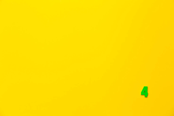 Nummer 4, vier, die vierte der babygrünen Plastikspielzeugnummer befindet sich in der unteren rechten Ecke auf einem gelben Papierhintergrund. Banner zum Thema Seitennummerierung, Timing oder Tag im Kalender. - Foto, Bild