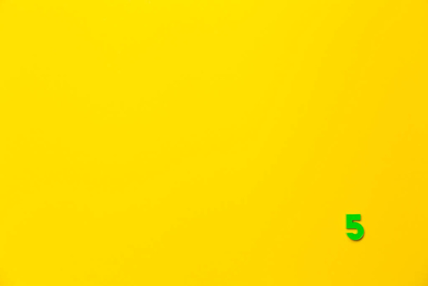 Número 5, cinco, o quinto do número de brinquedo verde bebê de plástico está localizado no canto inferior direito em um fundo de papel amarelo. Banner sobre o tema de numeração de páginas, tempo ou dia no calendário. - Foto, Imagem
