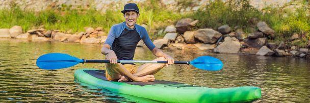 Joyful man is training SUP board in river on a sunny morning. Stand up paddle boarding - awesome active outdoor recreation BANNER, LONG FORMAT - Foto, Imagem