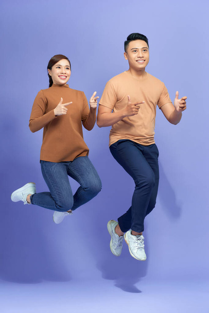 Отличное предложение. Положительная пара, прыгающая в воздух и указывающая на пространство для копирования на фиолетовом фоне - Фото, изображение