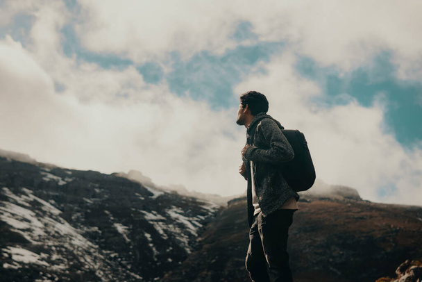 Άντρας με σακίδιο στέκεται στην ορεινή χώρα με τον ουρανό στο παρασκήνιο - Φωτογραφία, εικόνα