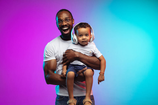 African-american father and son portrait on gradient studio background in neon - Fotografie, Obrázek