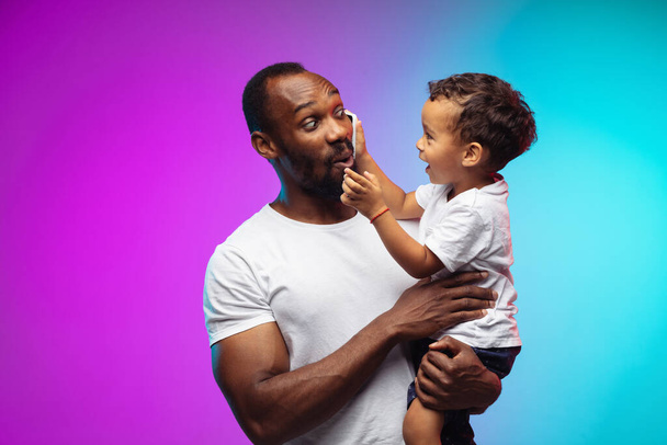 African-american father and son portrait on gradient studio background in neon - Foto, Imagen